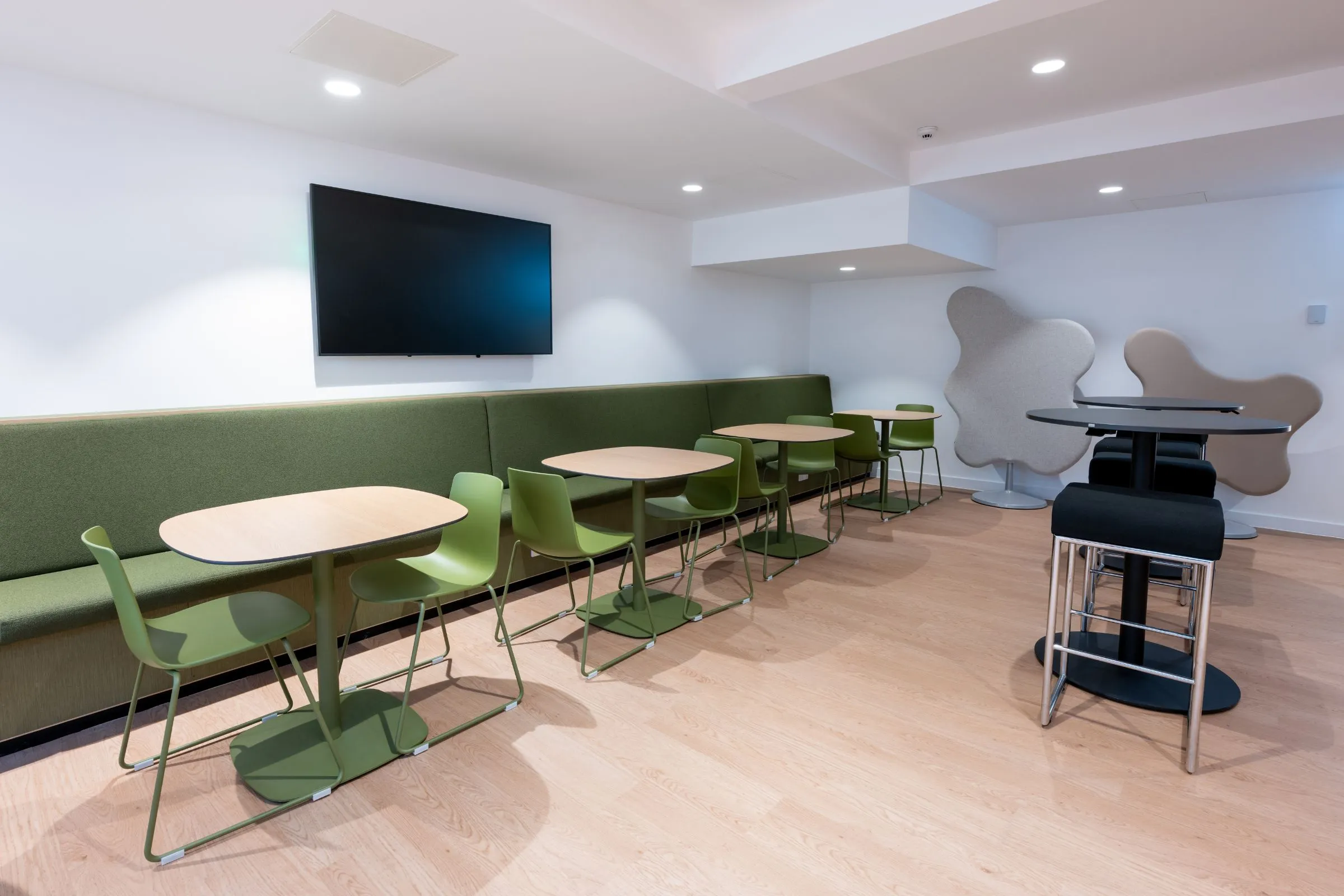 Breakout area at the Hutton Hub with green banquette seating, small tables and a wall-mounted screen